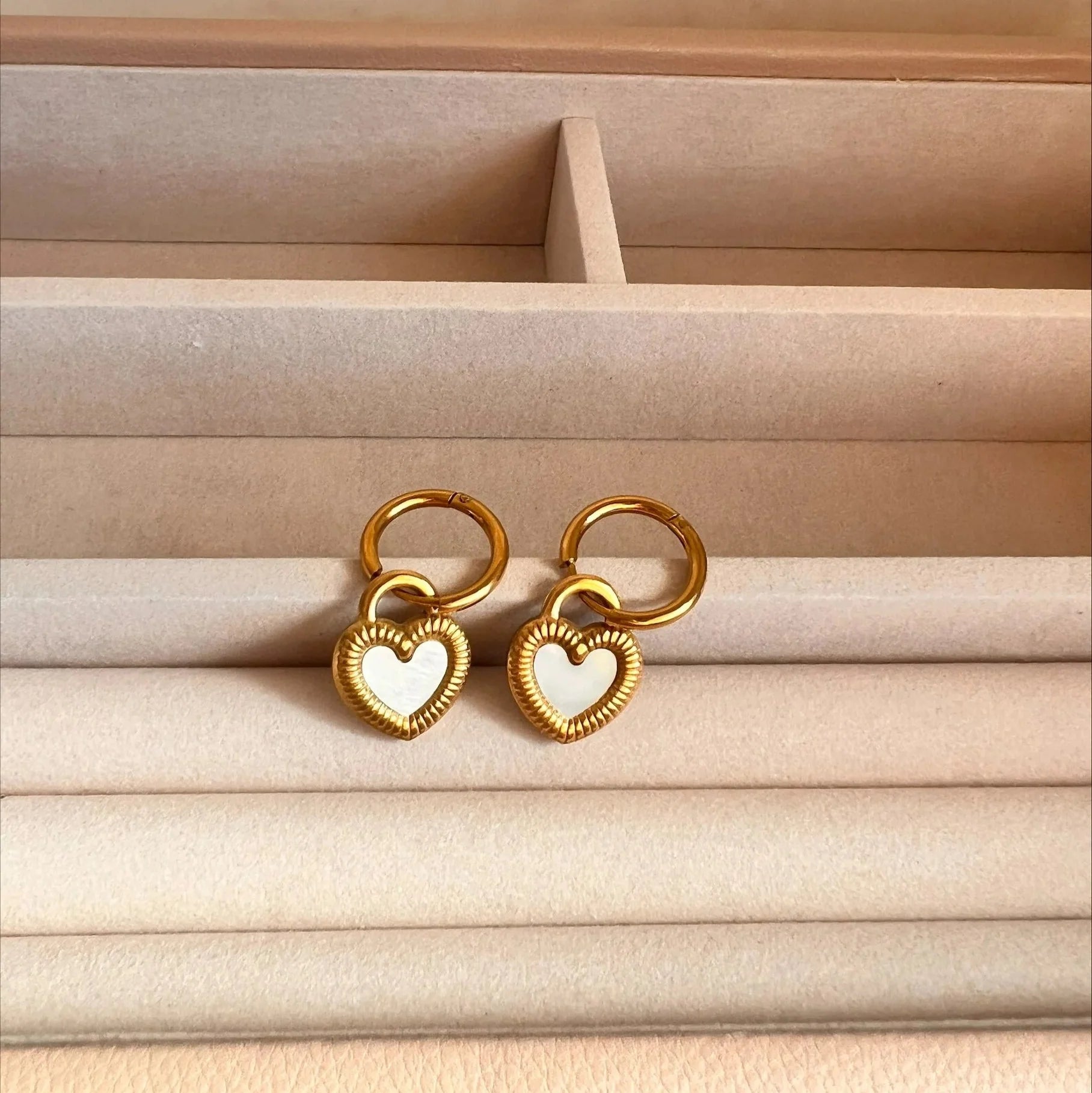 Gold heart-shaped earrings on a beige jewelry box