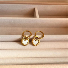 Gold heart-shaped earrings on a beige jewelry box