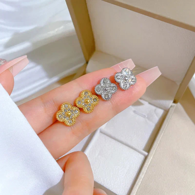 Gold and silver clover earrings held in a hand with a white background